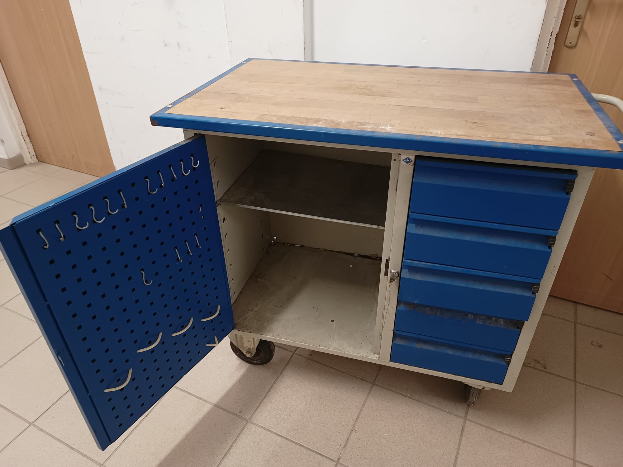 Zdjęcie przedstawia szafkę narzędziową koloru niebiesko-szarego z drewnianym blatem. Szafka używana w dobrym stanie.