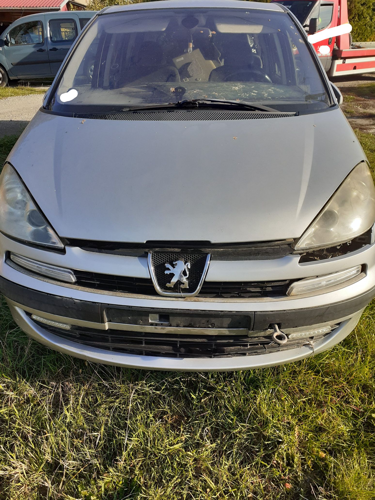 Maska srebrnego samochodu osobowego Peugeot typu minivan z uszkodzonym zderzakiem.