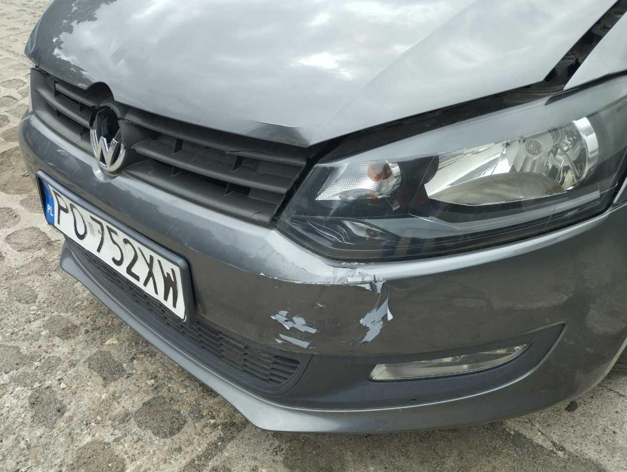 Krawędź maski nad reflektorem jest wygięta do góry, zderzak pęknięty, a lakier mocno się łuszczy i odpada.