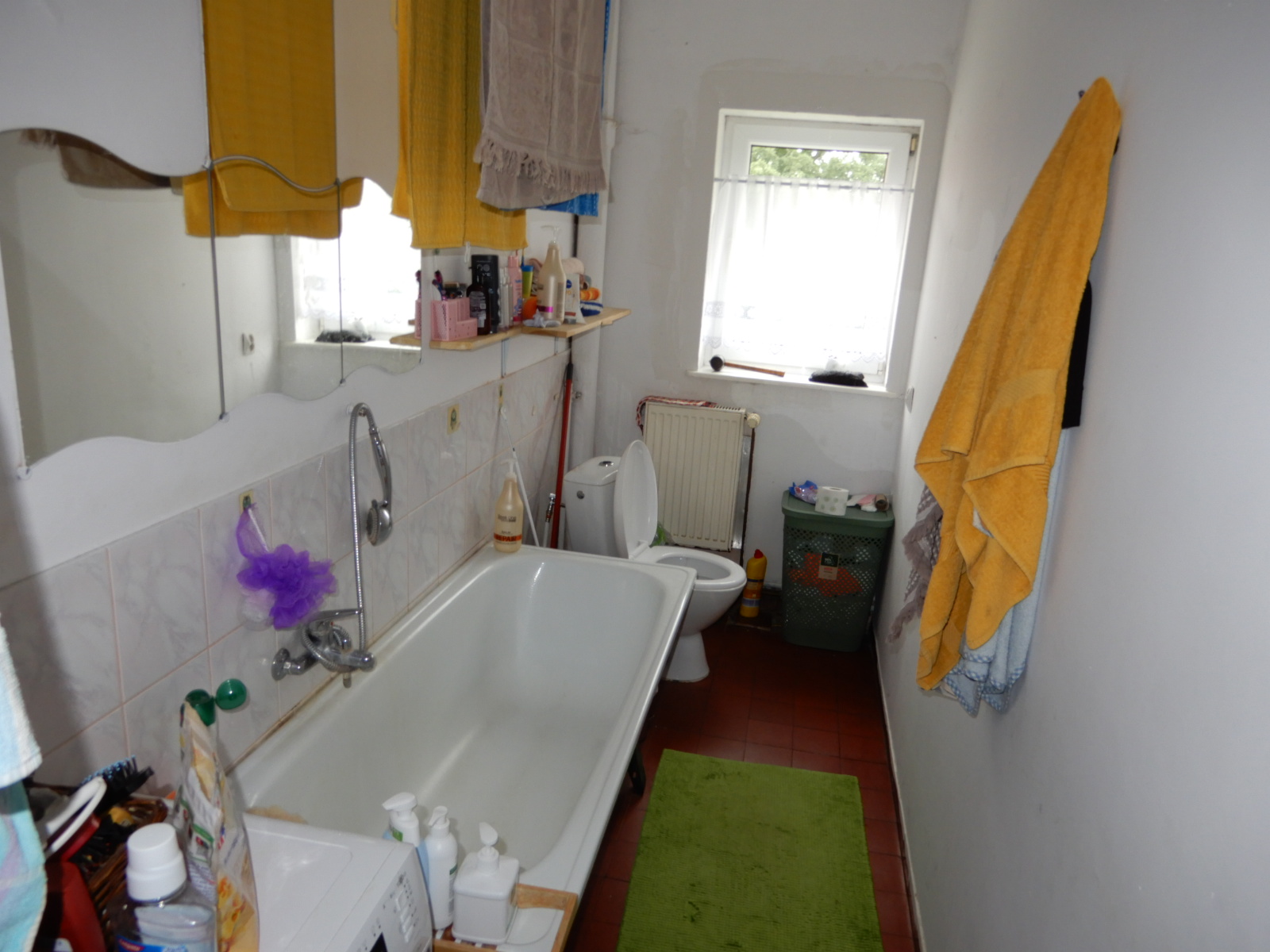 Widok łazienki z wc, na ścianach tynk malowany, na podłodze terakota (starego typu), nad wanną glazura