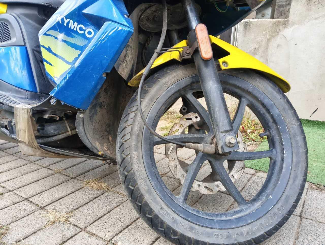Przednie koło pojazdu z oponą szosową, osłona motocykla z widocznymi zarysowaniami.