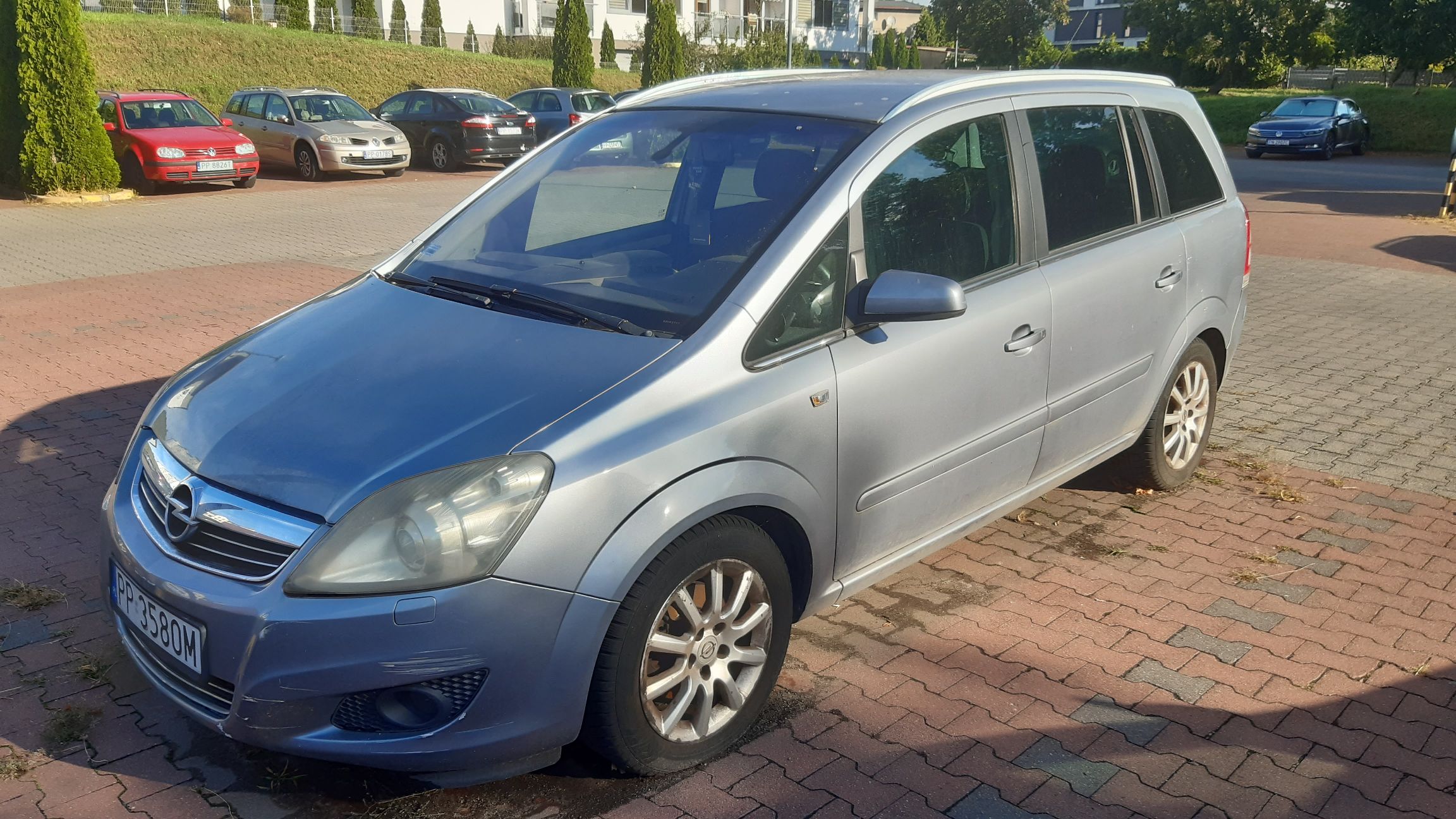 Srebrny samochód osobowy Opel Zafira, sfotografowany z przodu i z prawej strony