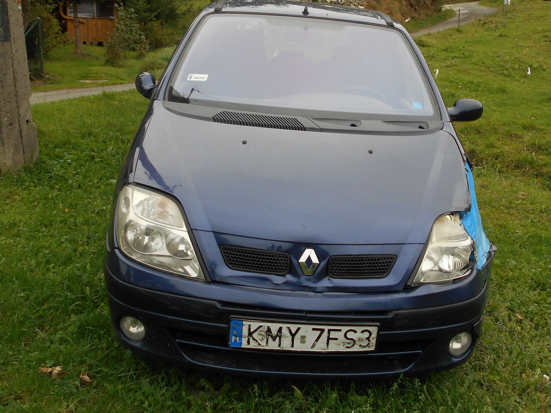 Przednia część ciemnoniebieskiego samochodu Renault z uszkodzonym prawym reflektorem.