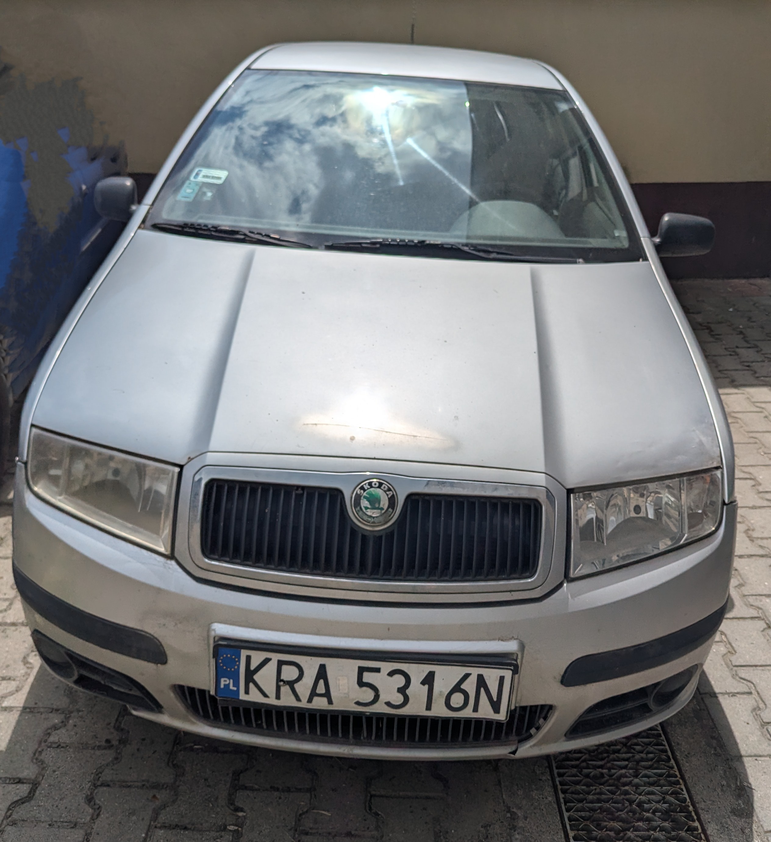 Przód srebrnego samochodu Skoda Fabia. Maska oraz zderzak posiadają oznaki napraw lakierniczych