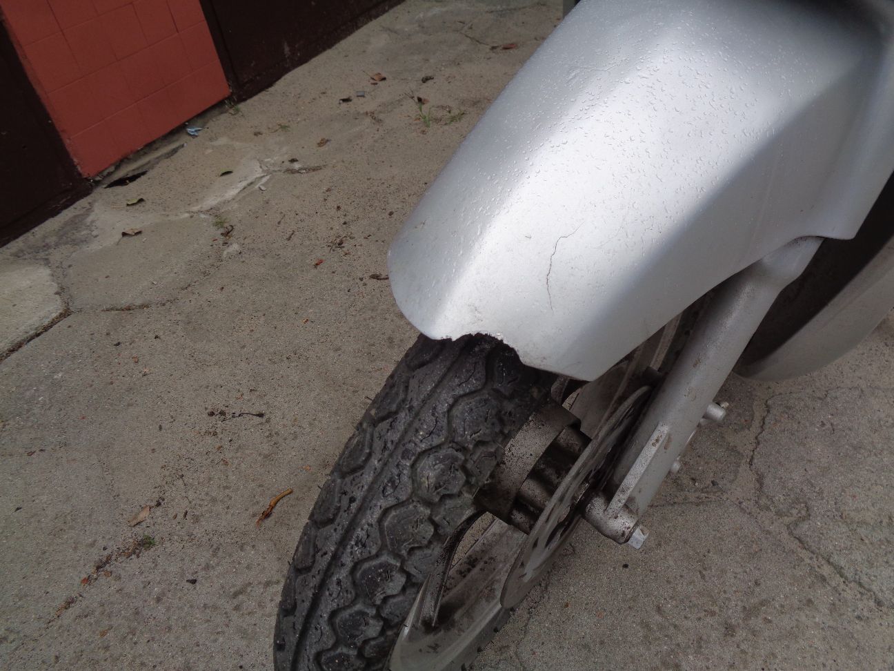 Przedni błotnik z widocznym pęknięciem i ubytkiem plastiku na krawędzi.