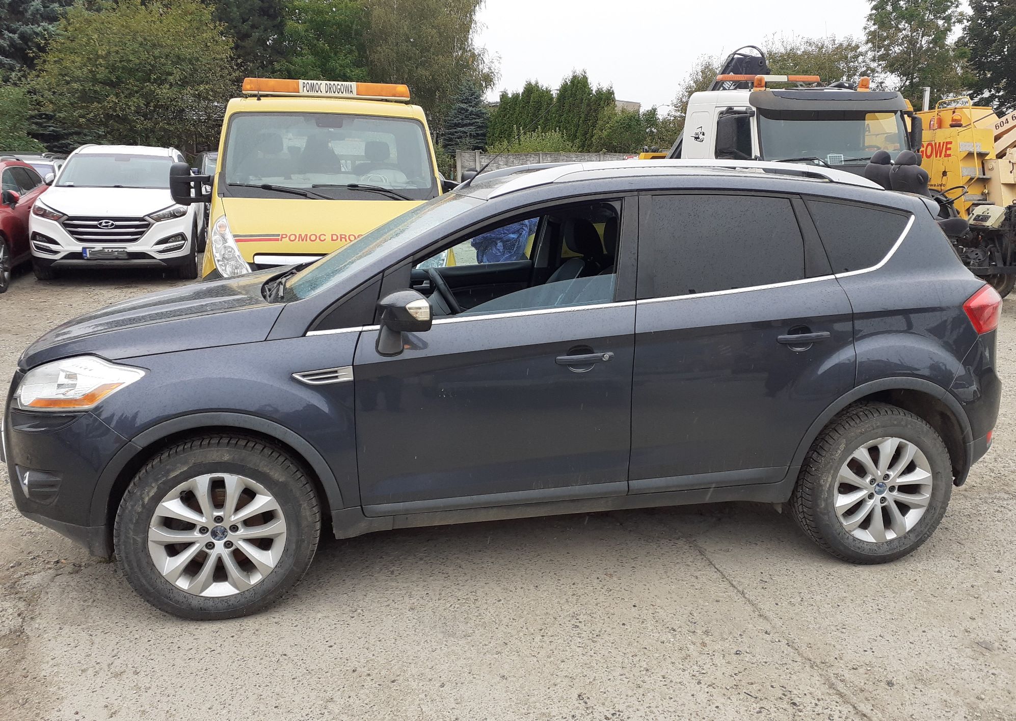 Czarny Ford Kuga widok z boku od strony kierowcy. Widoczne przyciemniane tylne szyby, aluminiowe koła i srebrne relingi dachowe.