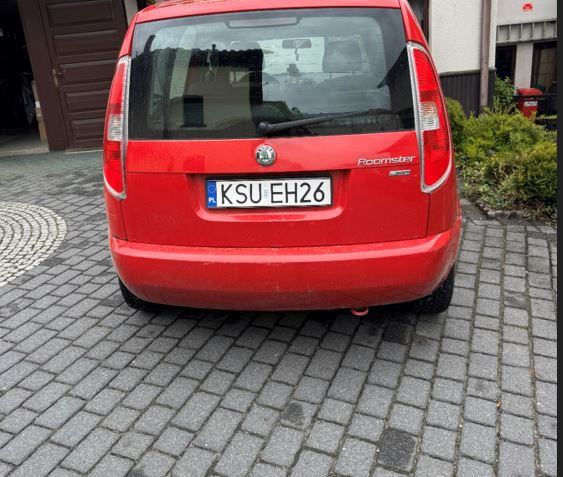 Tył samochodu marki Skoda Roomster w wyrazistym czerwonym kolorze. Zdjęcie centralne ukazuje zamkniętą klapę bagażnika.