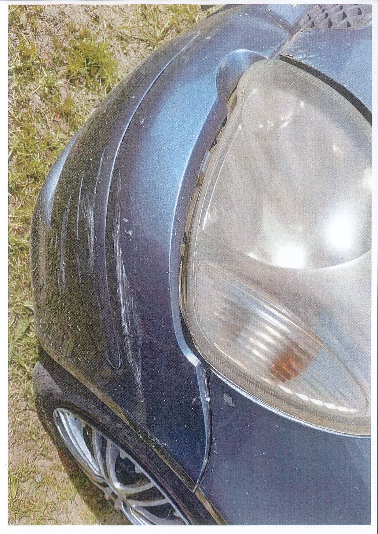 Przednia lewa lampa samochodu osobowego TOYOTA YARIS i część mocno porysowanego zderzaka. Widoczna korozja blachy.
