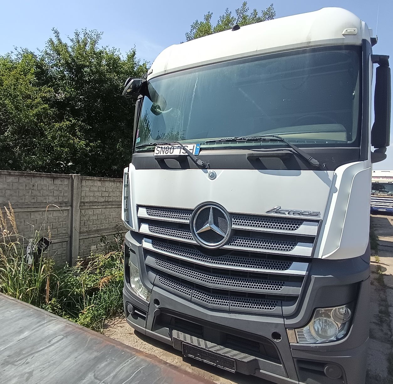 Biały ciągnik siodłowy ciężarowy widziany z przodu. Charakterystyczny grill z dużym logo marki Mercedes.