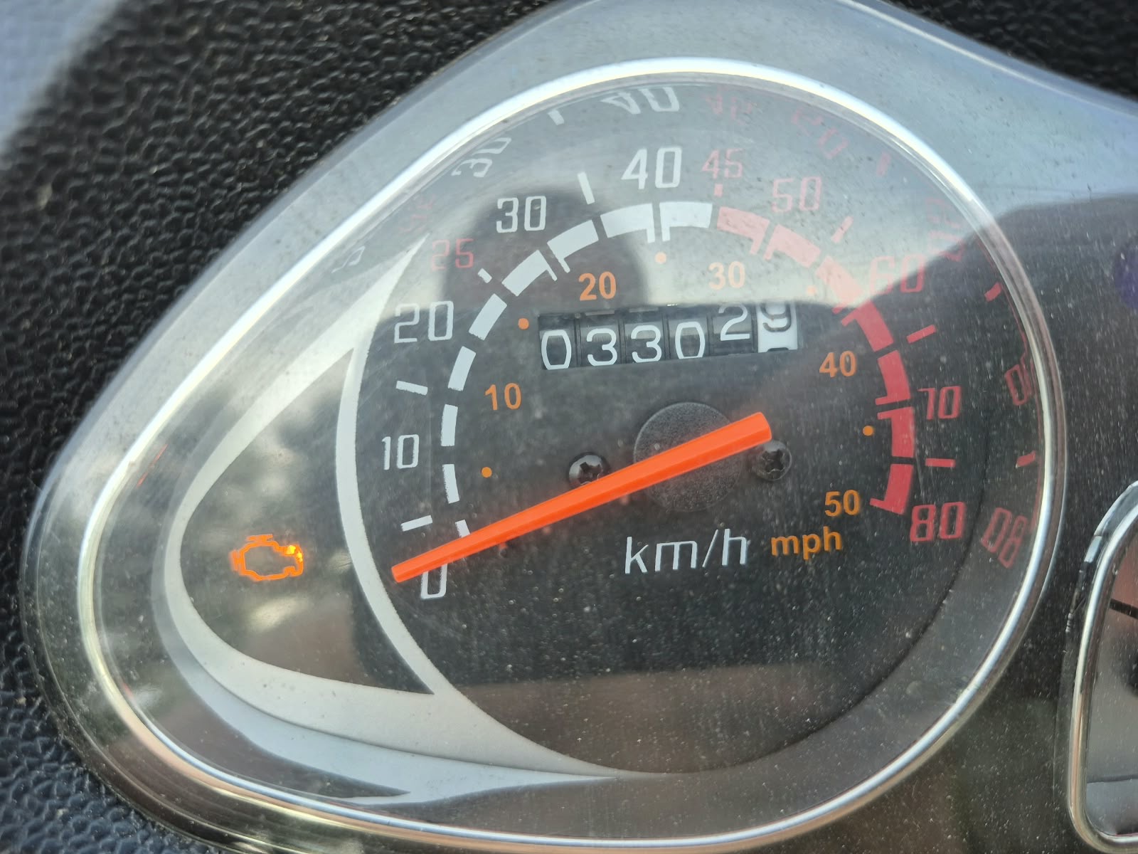 Analogowy licznik skutera wskazujący przebieg 3302 km, z widoczną pomarańczową kontrolką silnika (check engine)