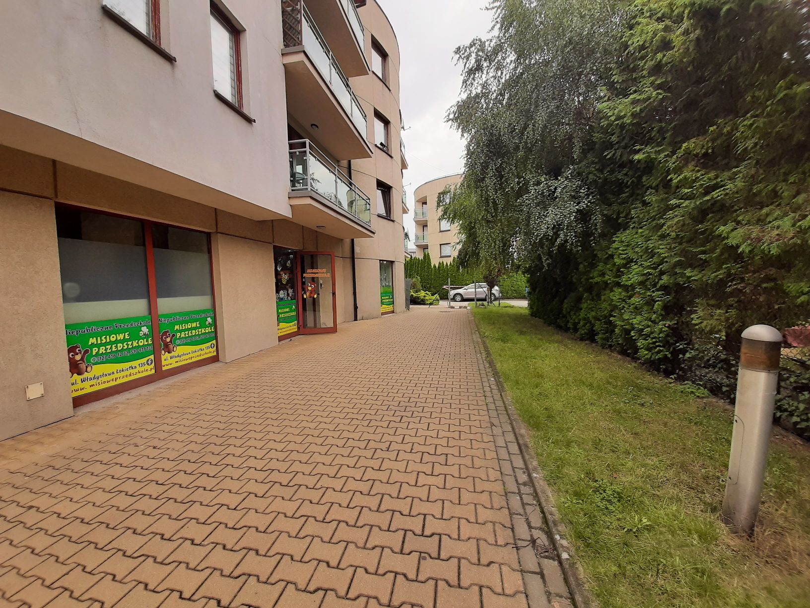 Lokal usługowy na parterze 4 kondygnacyjnego budynku. Widok boczny budynku wraz z jego otoczeniem.