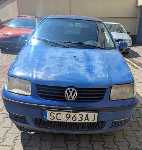 Przód niebieskiego pojazdu VOLKSWAGEN POLO. Duże ubytki lakieru na masce pojazdu, lampy zmatowione