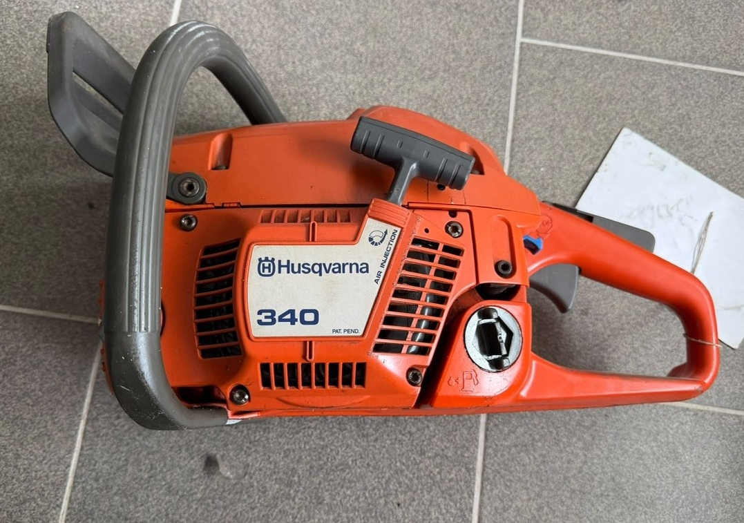 Pomarańczowa pilarka spalinowa Husqvarna bez prowadnicy i łańcucha, widok z boku.