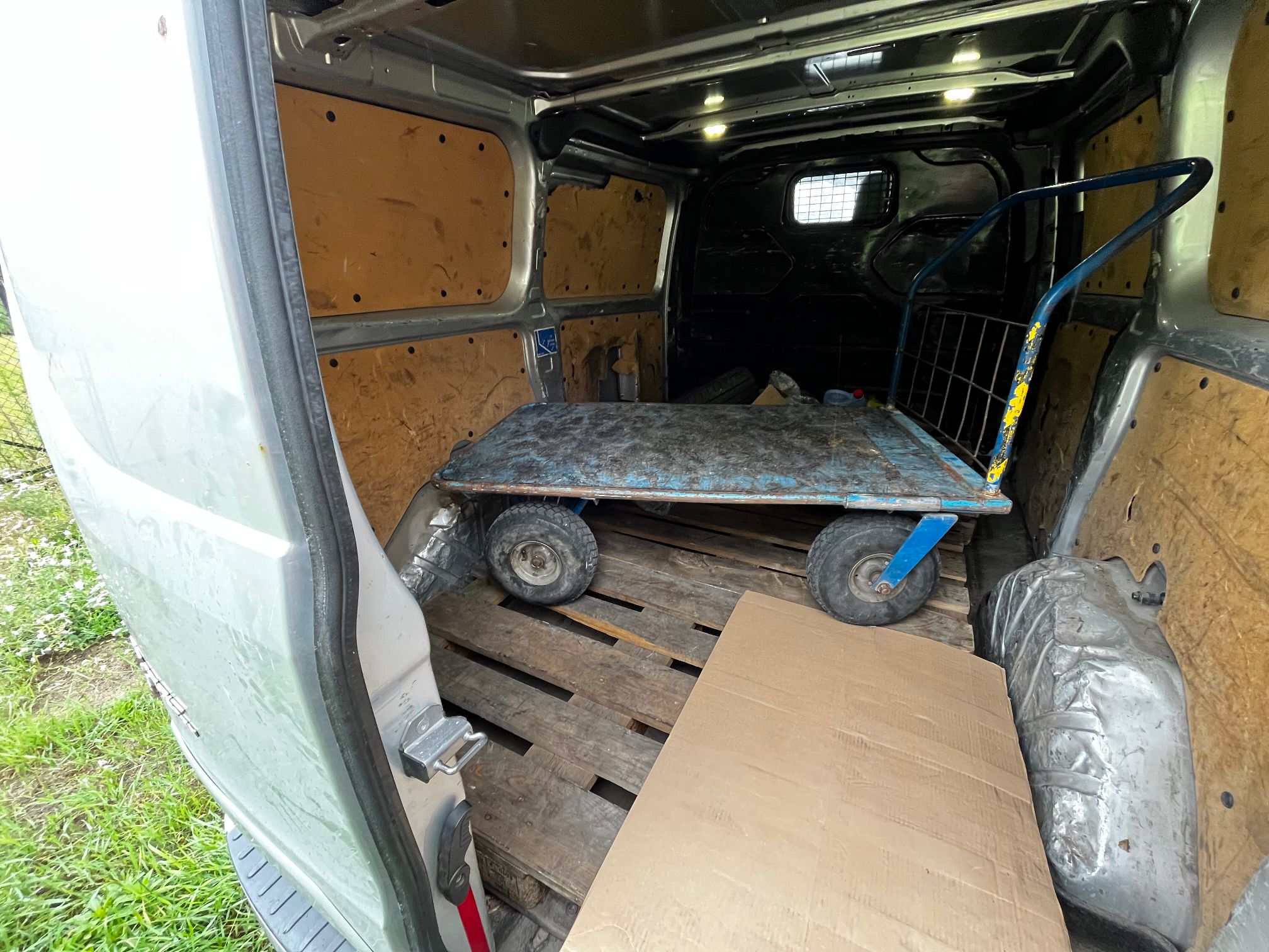 srebrny Ford Transit Custom pokazany luk bagażowy w którym znajduje się wózek towarowy