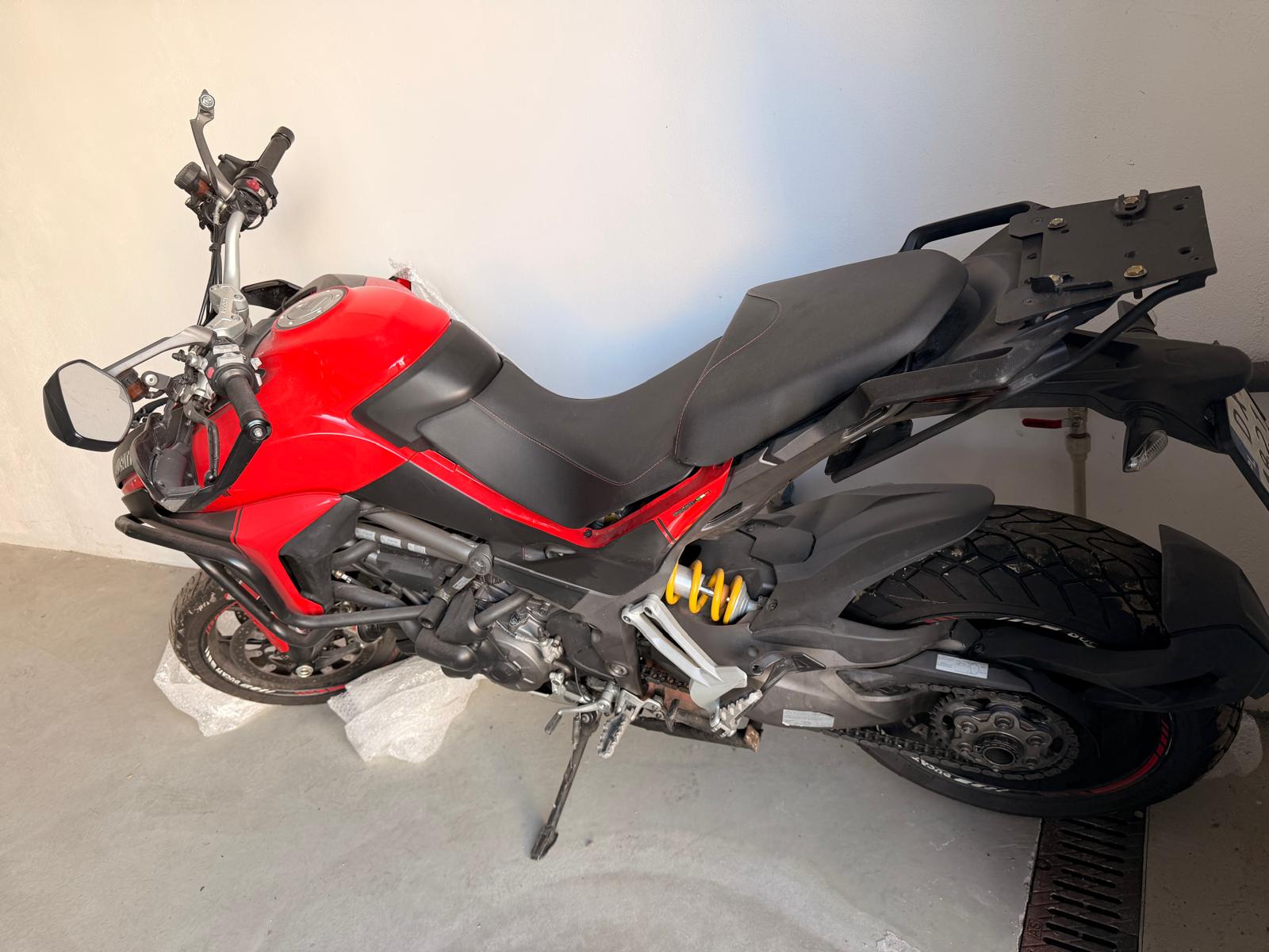 Lewy bok czerwonego Ducati Multistrada. Motocykl stojący na bocznej stopce w garażu.