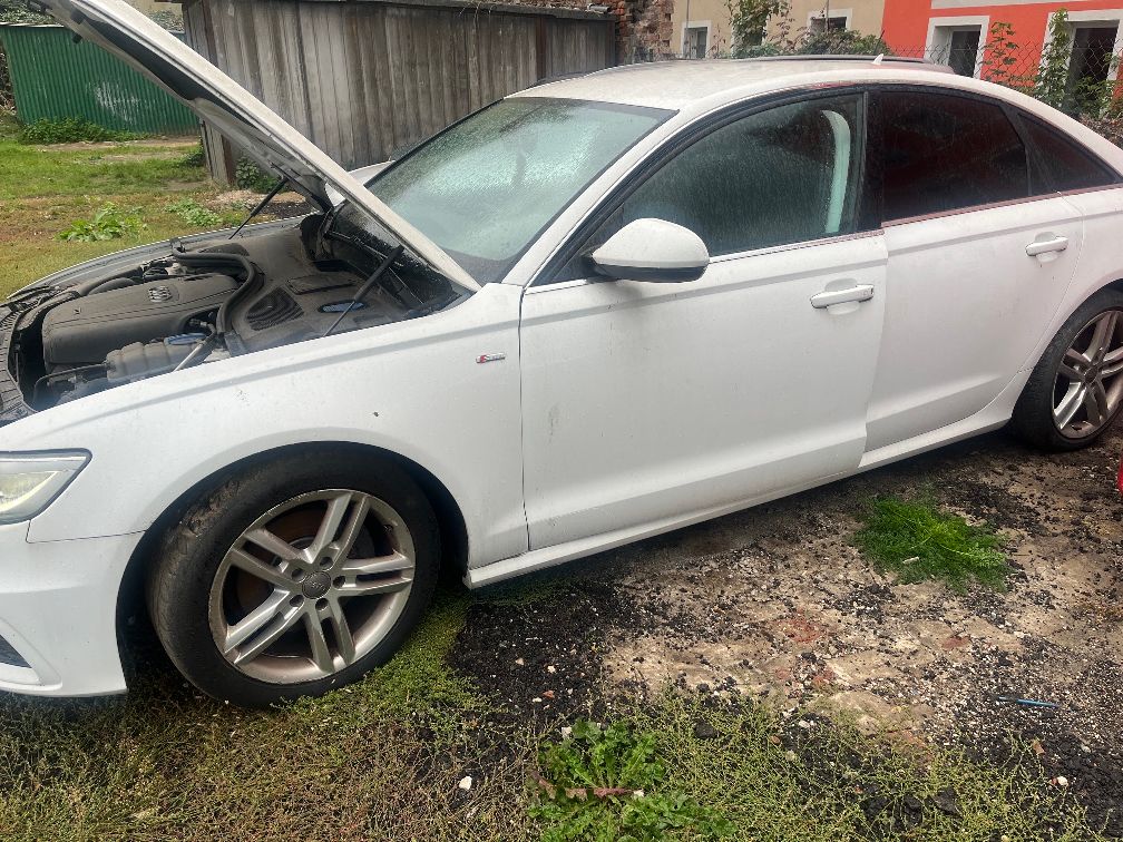 Białe Audi A6 z otwartą maskę silnika. Na przednim błotniku widoczny jest znaczek S-line.