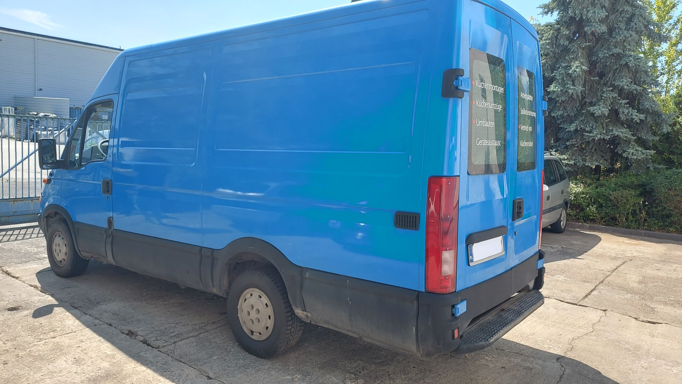 Tył i lewy bok jasnoniebieskiego furgonu Iveco Daily.