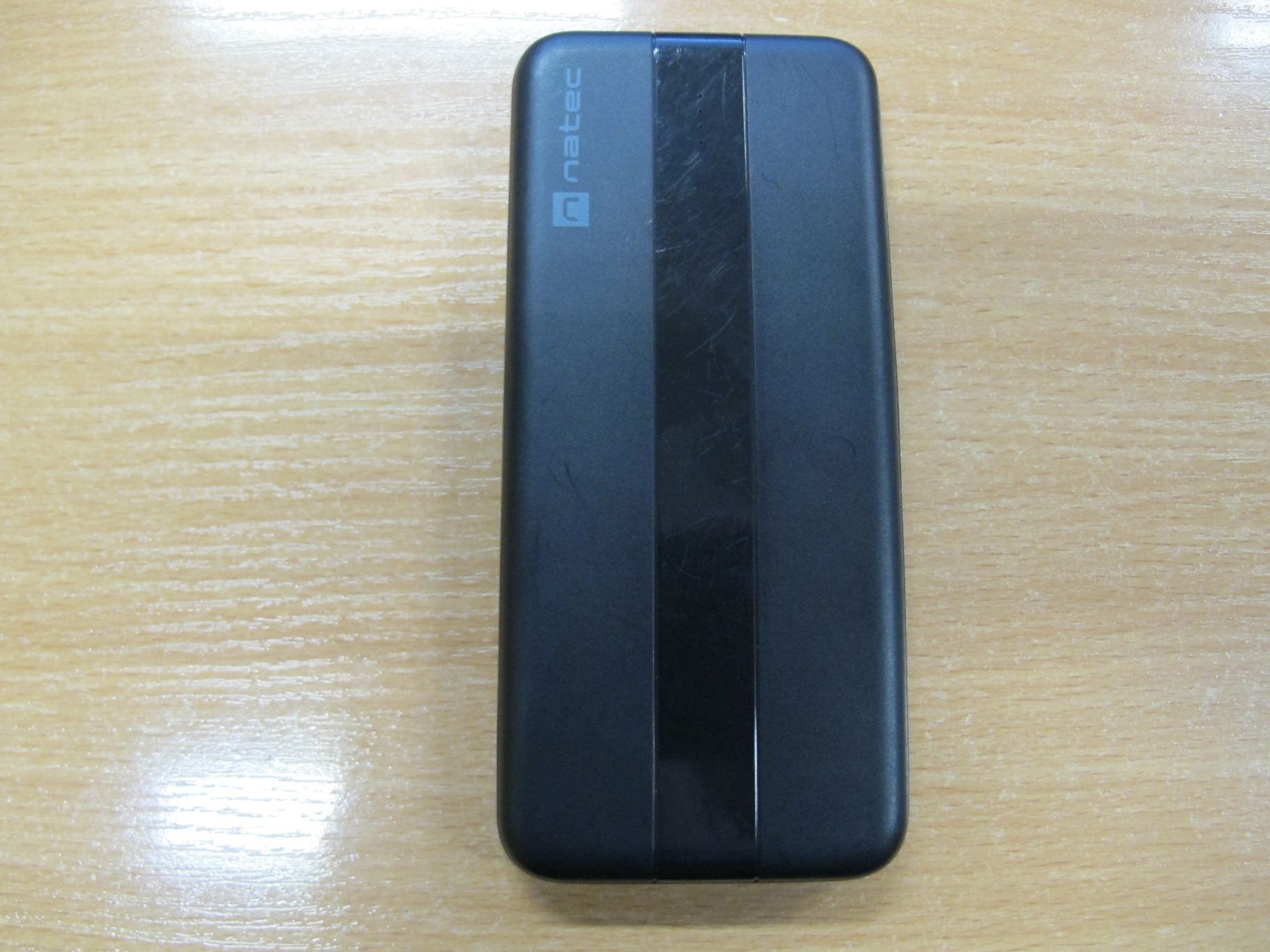 Widok z góry na czarny powerbank z błyszczącym paskiem na obudowie.
