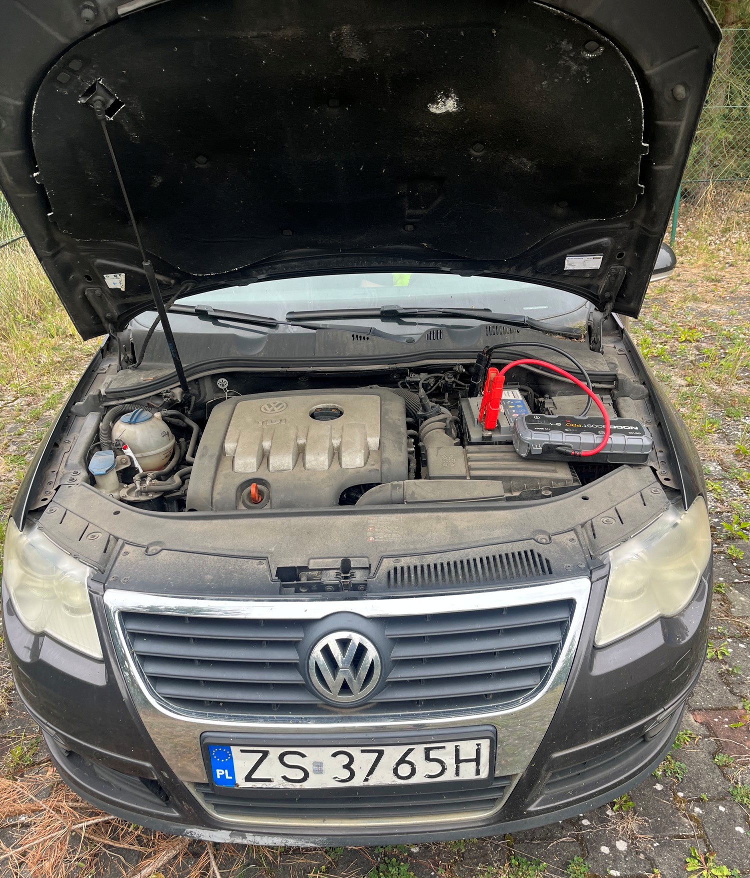 Widok otwartej komory silnika Volkswagena Passata z podłączonym do akumulatora szarym powerbankiem rozruchowym.