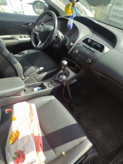 Wnętrze samochodu marki Honda z kierownicą po lewej stronie, ciemną materiałową tapicerką oraz manualną skrzynią biegów.