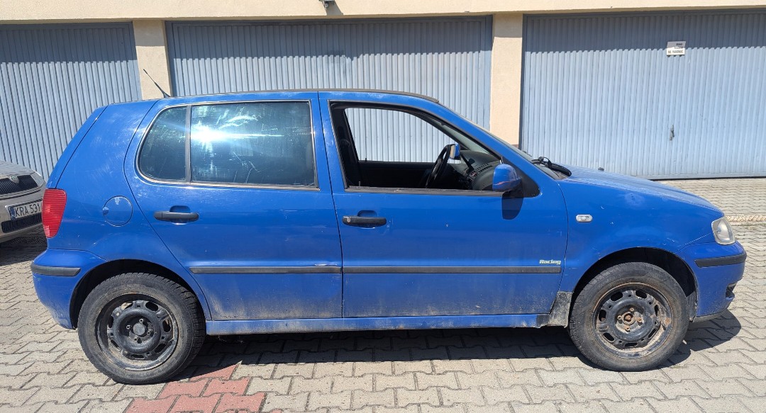 Prawy bok niebieskiego pojazdu VOLKSWAGEN POLO. Na szybie tylnych drzwi założona folia przyciemniająca, korozja na progu