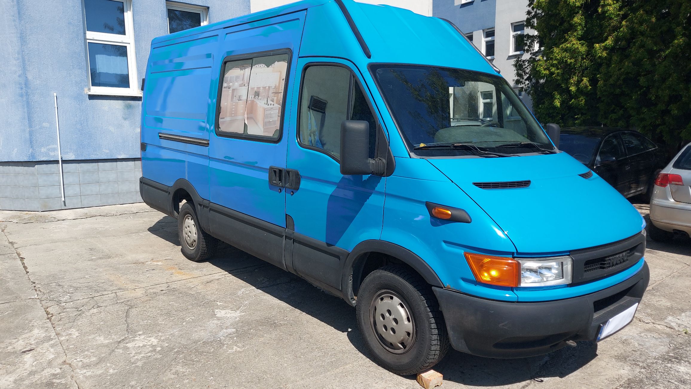 Przód i prawy bok niebieskiego dostawczego Iveco Daily z oknem w drzwiach przesuwnych.