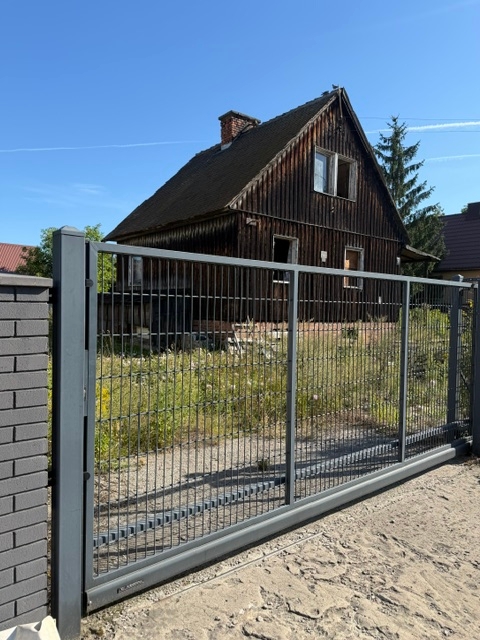 Dom typu fińskiego w złym stanie technicznym, z metalowym ogrodzeniem z przesuwną bramą.