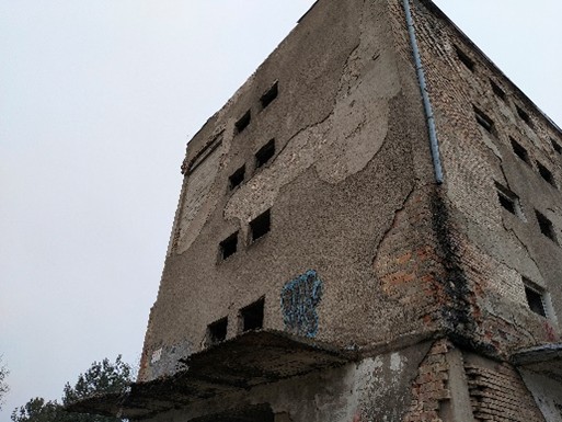 Zniszczony, opuszczony budynek z cegły i betonu, z popękanymi ścianami, bez okien.