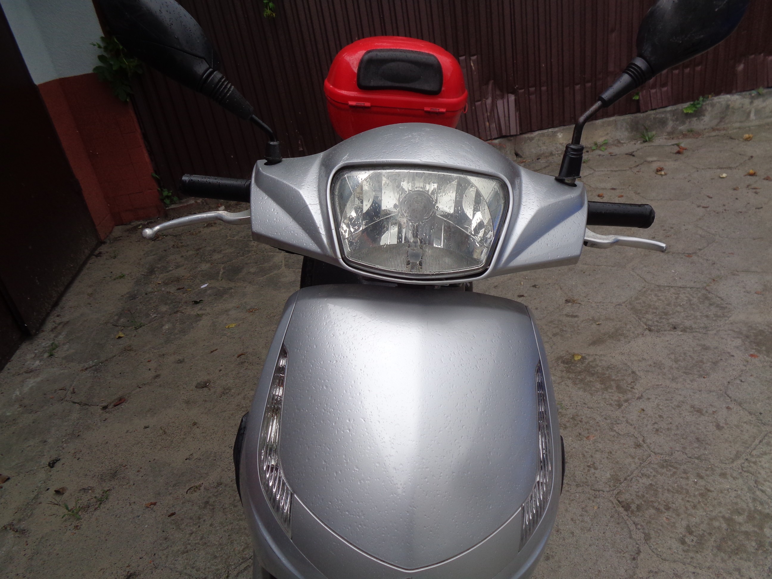 Przód motoroweru, widoczny reflektor i kierownica, matowy, porysowany plastik przedniej obudowy.