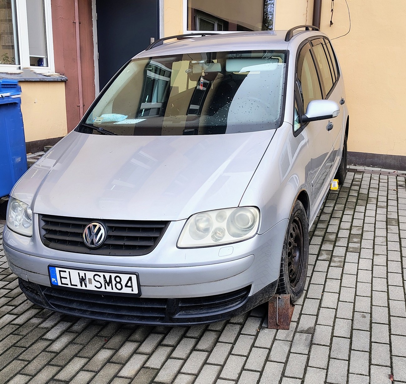 Srebrny samochód osobowy. Na dachu widoczne są czarne relingi dachowe. Z przodu chromowane logo producenta.