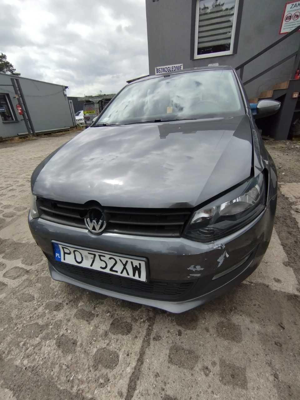 Pięciodrzwiowy Volkswagen Polo hatchback w ciemnoszarym metalicznym kolorze z uszkodzonym błotnikiem, zderzakiem i maską.