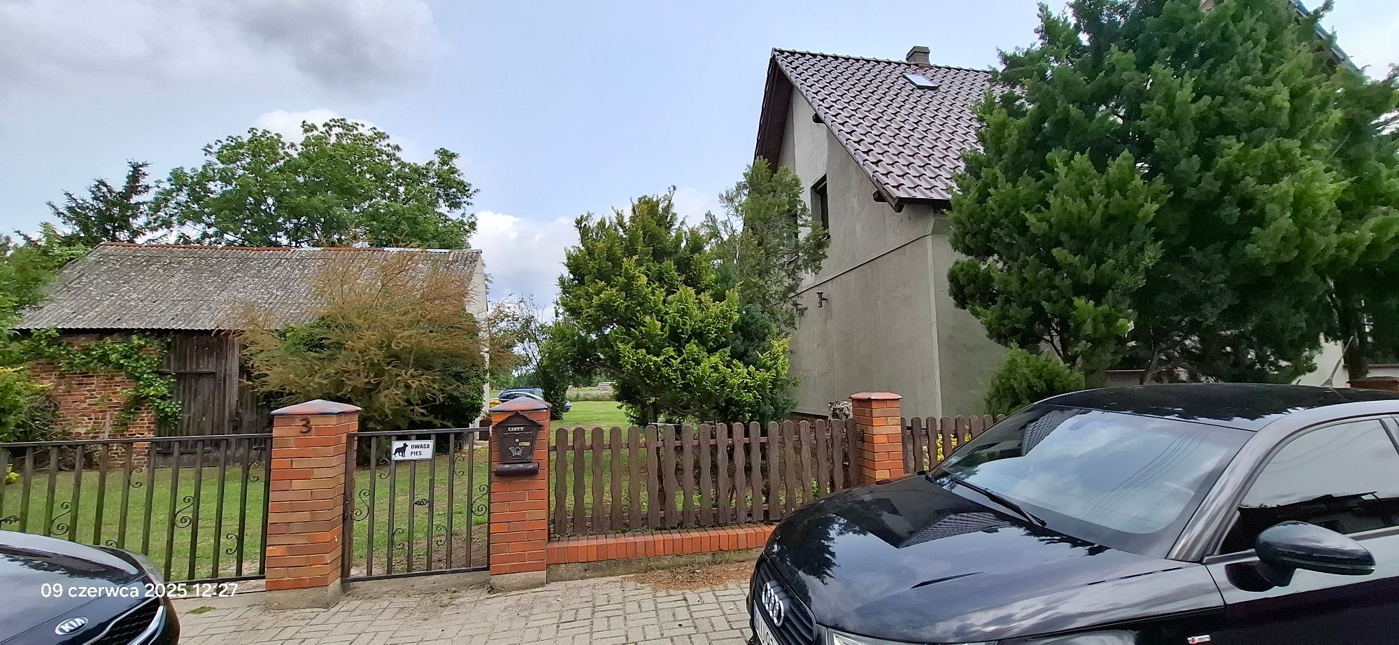 Po lewej stronie stodoła po prawej lewy bok domu jednorodzinnego, bramka wejściowa na wprost.