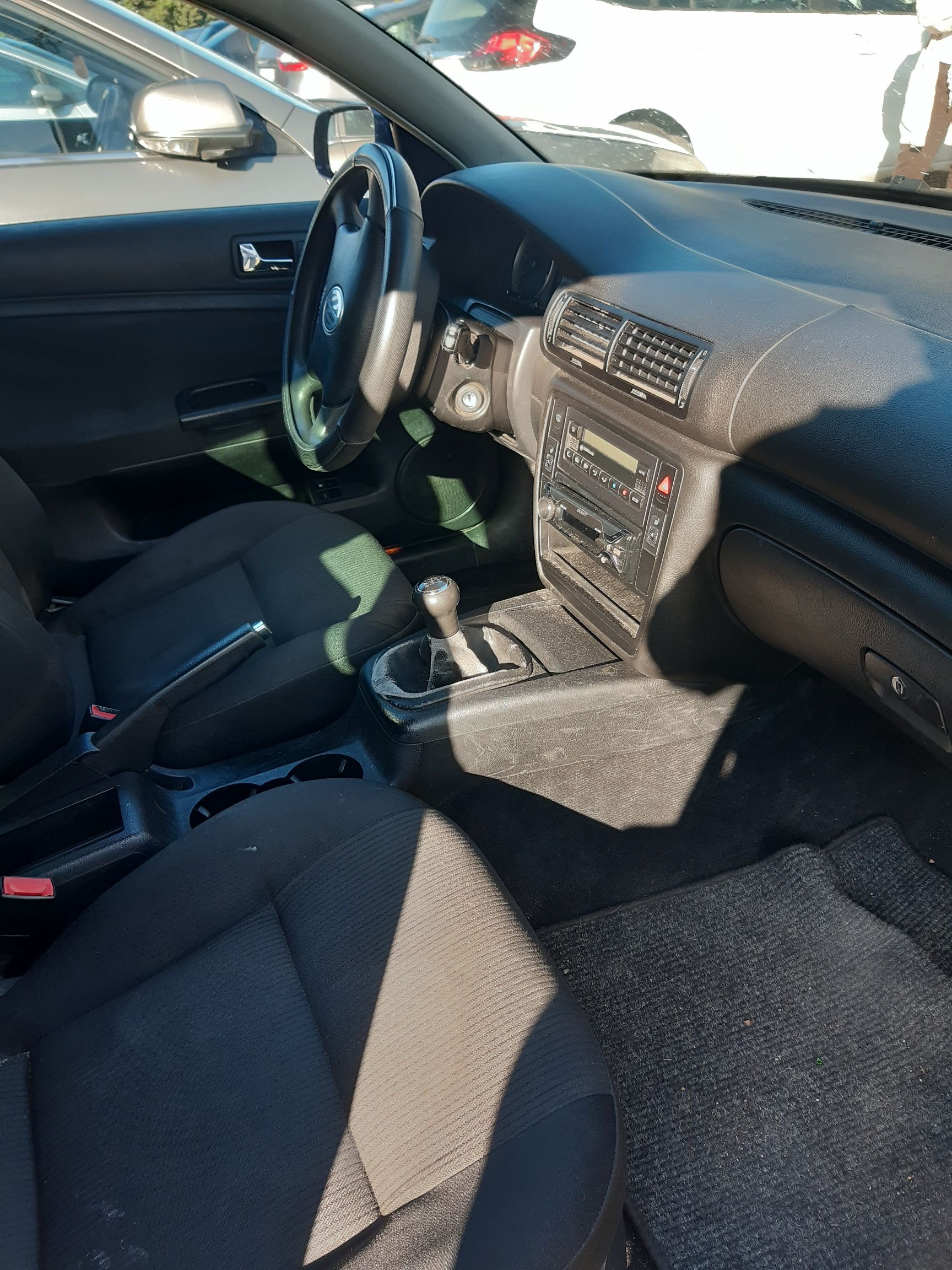 Wnętrze Volkswagena Passata B5 z ciemną materiałową tapicerką, kierownicą, konsolą środkową i manualną skrzynią biegów.