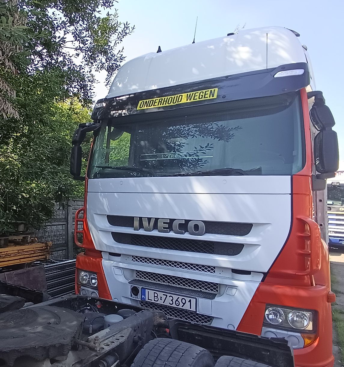 Biało-pomarańczowy samochód ciężarowy-skrzynia, widok z przodu. Widoczne duże logo marki IVECO.