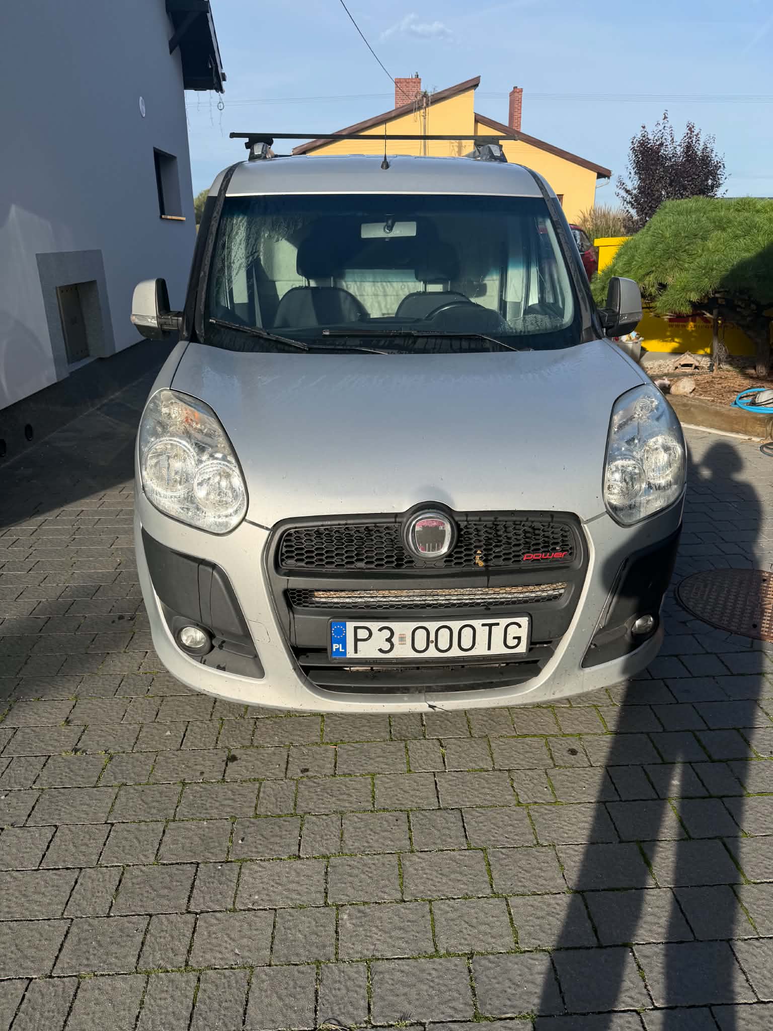 Fiat Doblo z 2010 roku o charakterystycznej bryle. Auto ma dużą przednią szybę, pionowe reflektory i przesuwne drzwi boczne.