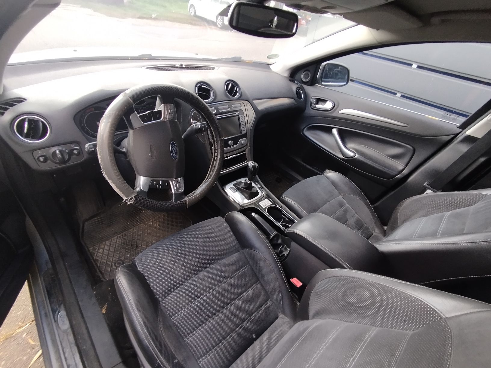 Wnętrze Forda Mondeo z widocznymi przednimi fotelami z ciemną tapicerką, kierownicą oraz deską rozdzielczą.