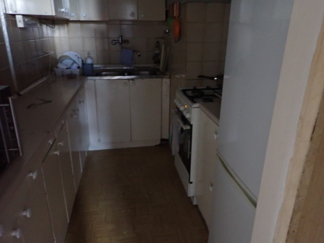 Ciemna, wąska kuchnia z płytkami na ścianach, na podłodze parkiet, wyposażona w agd oraz meble kuchenne
