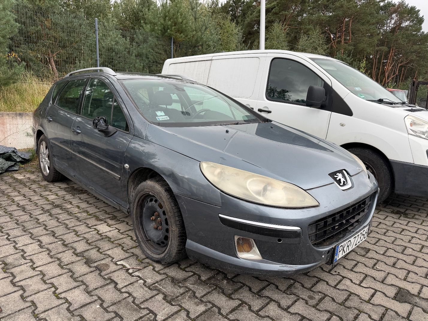 Szary Peugeot 407 SW, widok prawego boku, przednia stalowa felga bez kołpaka, srebrne relingi dachowe, uszkodzone lusterko.