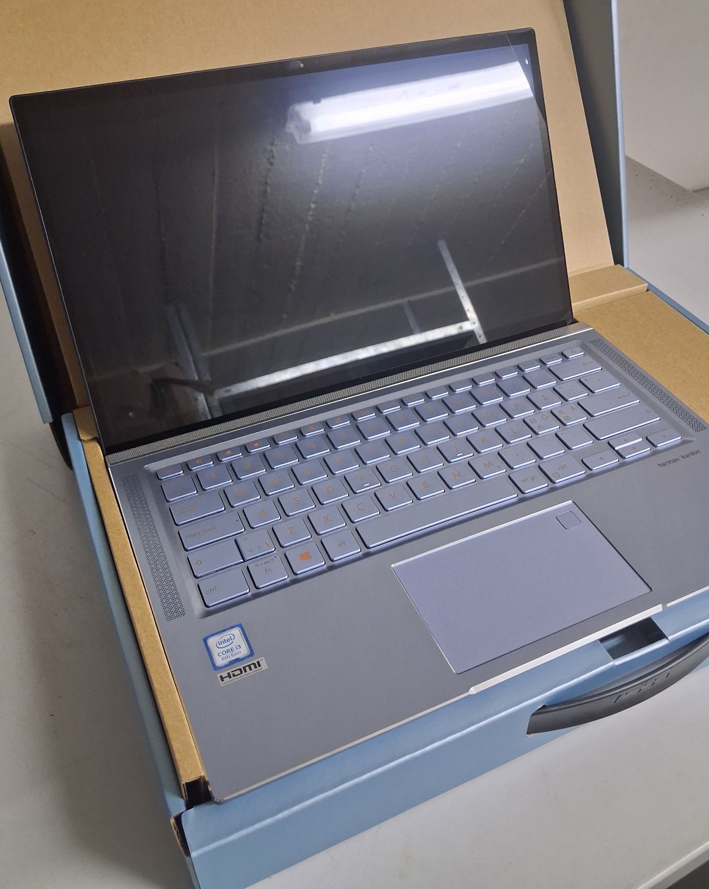 Laptop z otwartym monitorem i widoczną klawiaturą w opakowaniu kartonowym.
