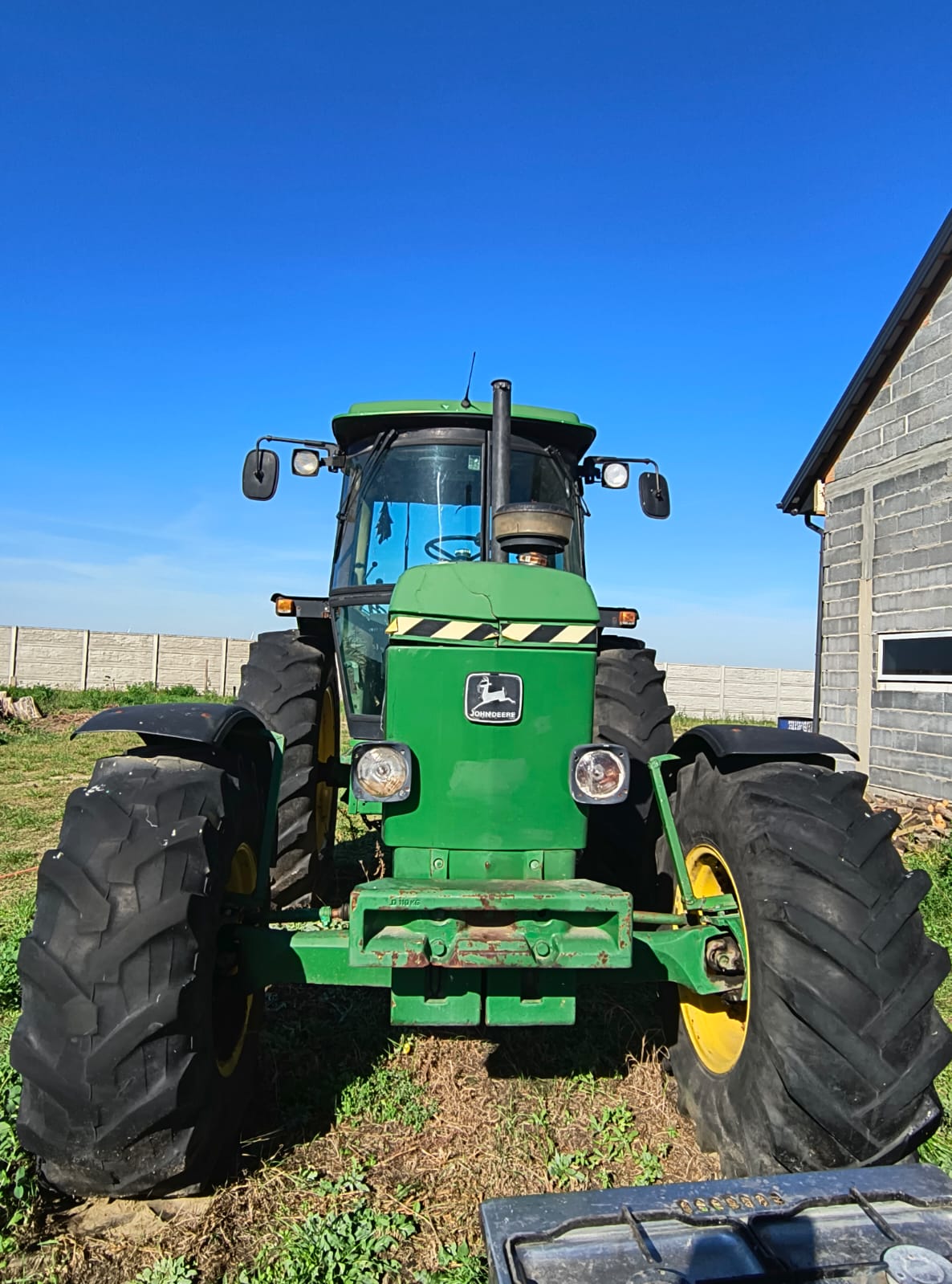 Zdjęcie przedstawia zielono-żółty ciągnik rolniczy marki John Deere, sfotografowany od przodu