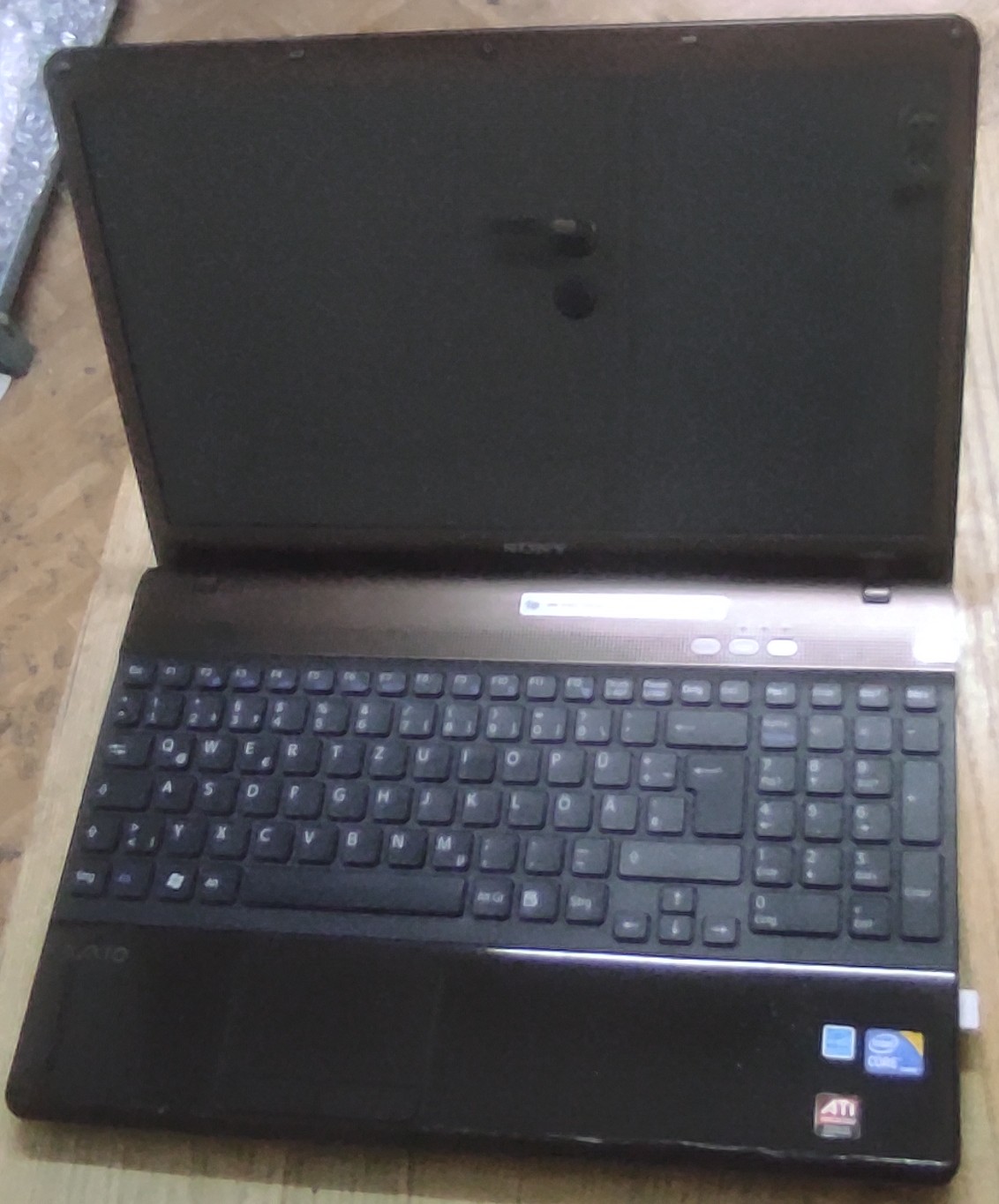 Otwarty laptop z widoczną klawiaturą, touchpad ze znacznymi śladami użytkowania.