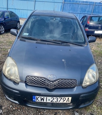 Granatowy samochód widziany z przodu, z widoczną tablicą rejestracyjną i znaczkiem toyota