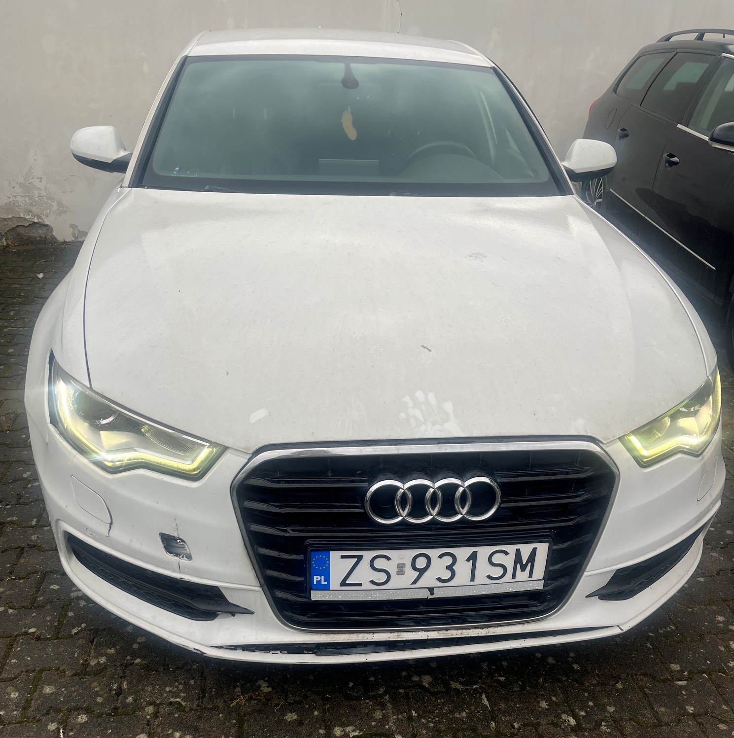 Przód białego Audi A6 z widocznymi uszkodzenia po prawej stronie przedniego zderzaka.