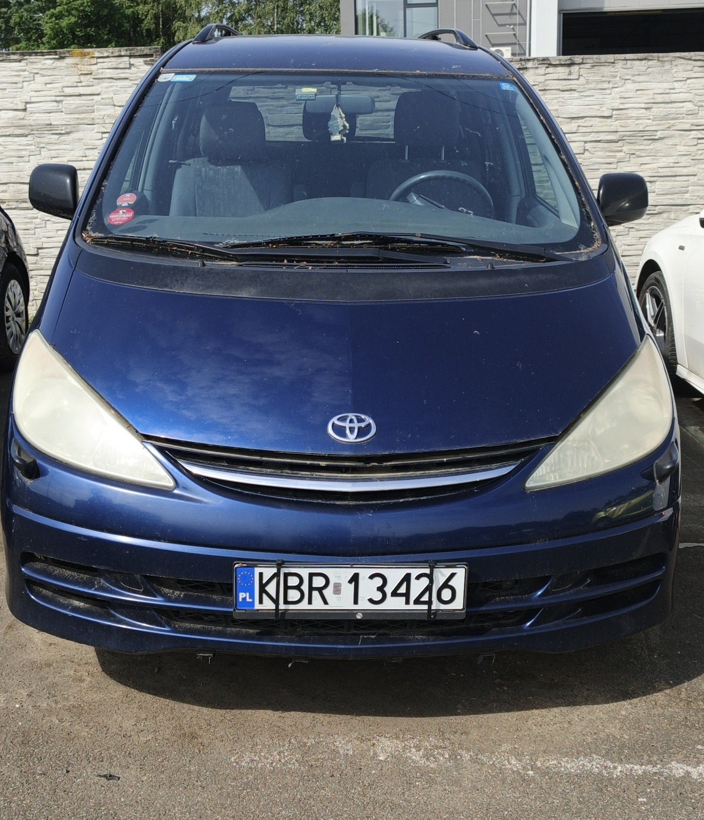 Przód samochodu Toyota Previa wraz z tablicą rejestracyjną KBR 13426. Kolor pojazdu granatowy.