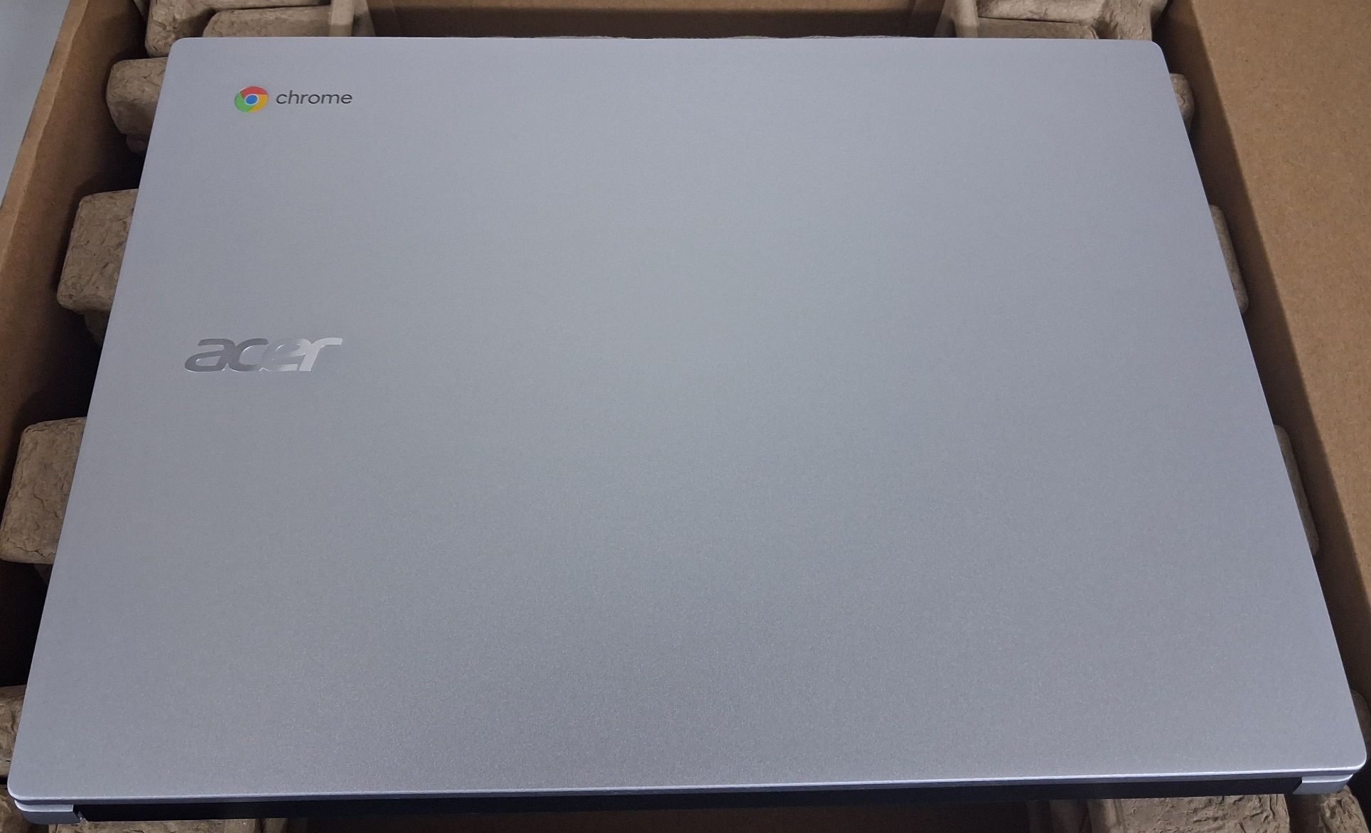 Laptop koloru srebrnego z napisem Acer w opakowaniu kartonowym koloru brązowego.