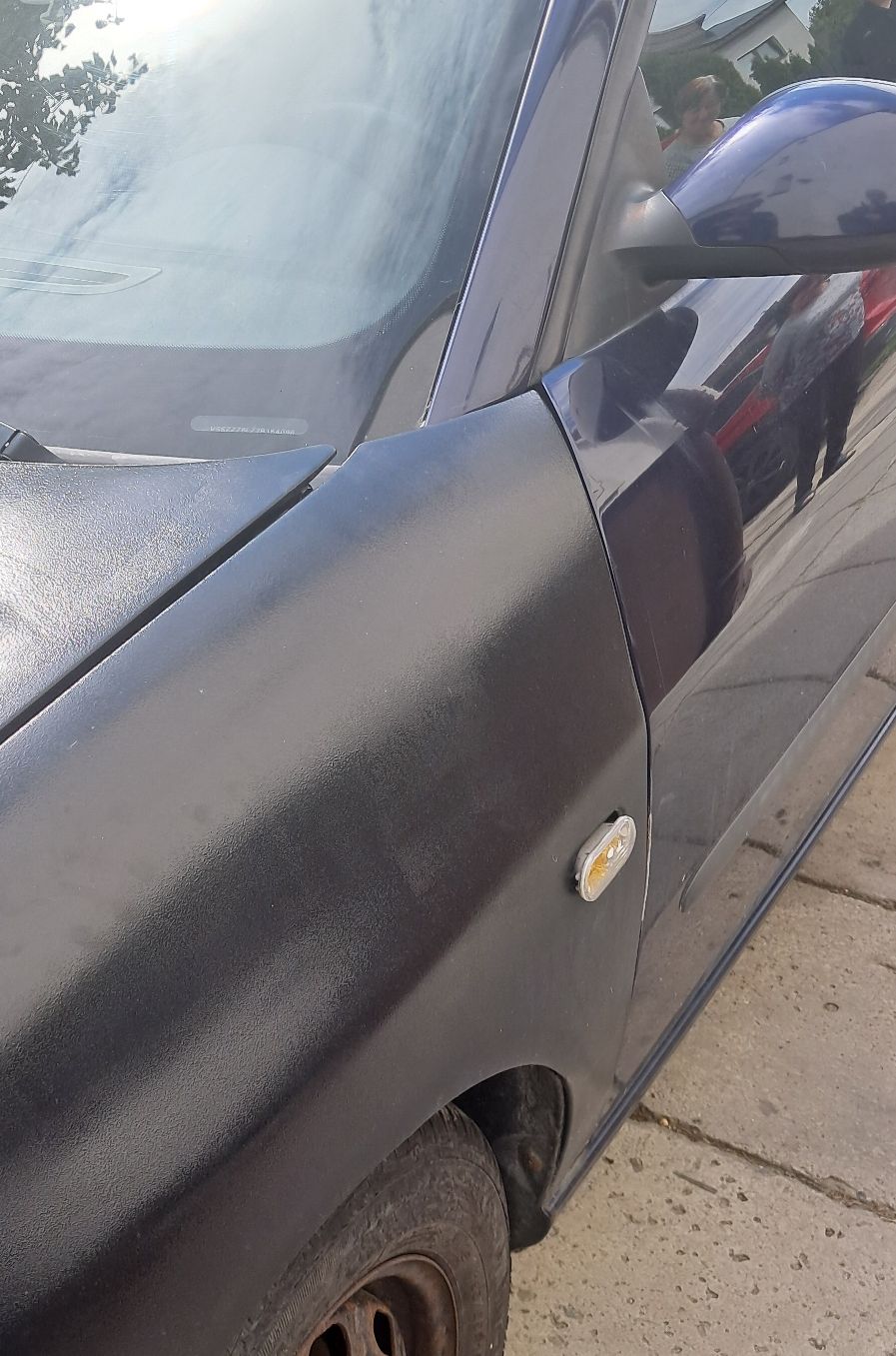 Fragment przednich lewych drzwi koloru granatowego oraz fragment maski koloru czarnego matowego samochodu Seat Ibiza