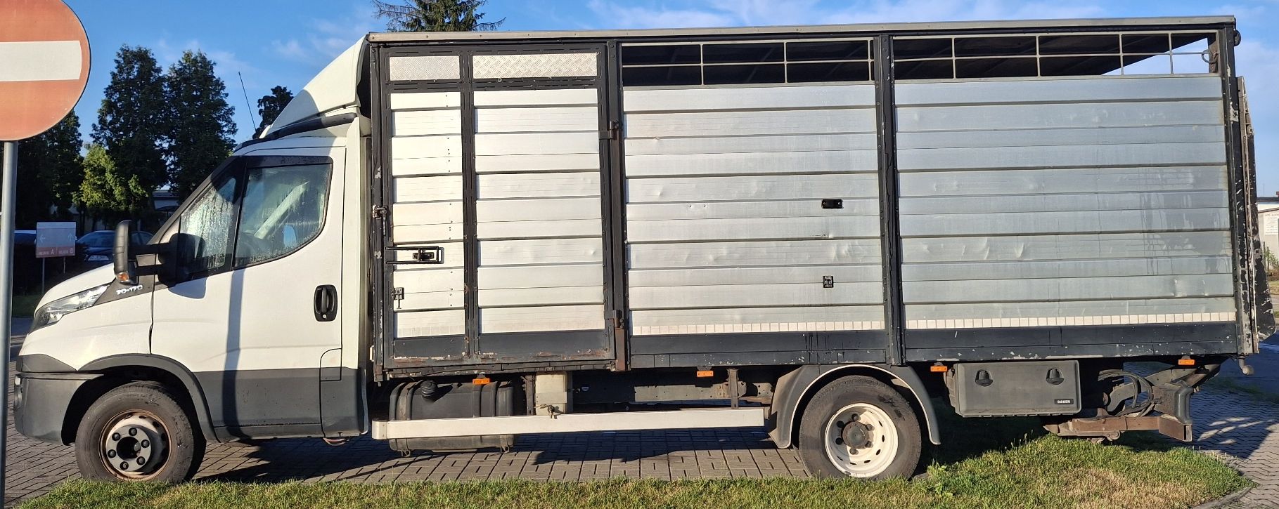Białe Iveco Daily z lewego profilu. Duża zabudowa do przewozu zwierząt.