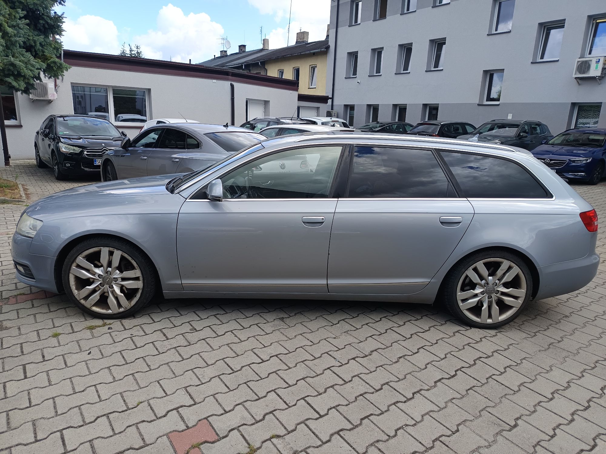 Srebrne Audi A6 Avant (kombi) widoczne z boku, zaparkowane na kostce brukowej.