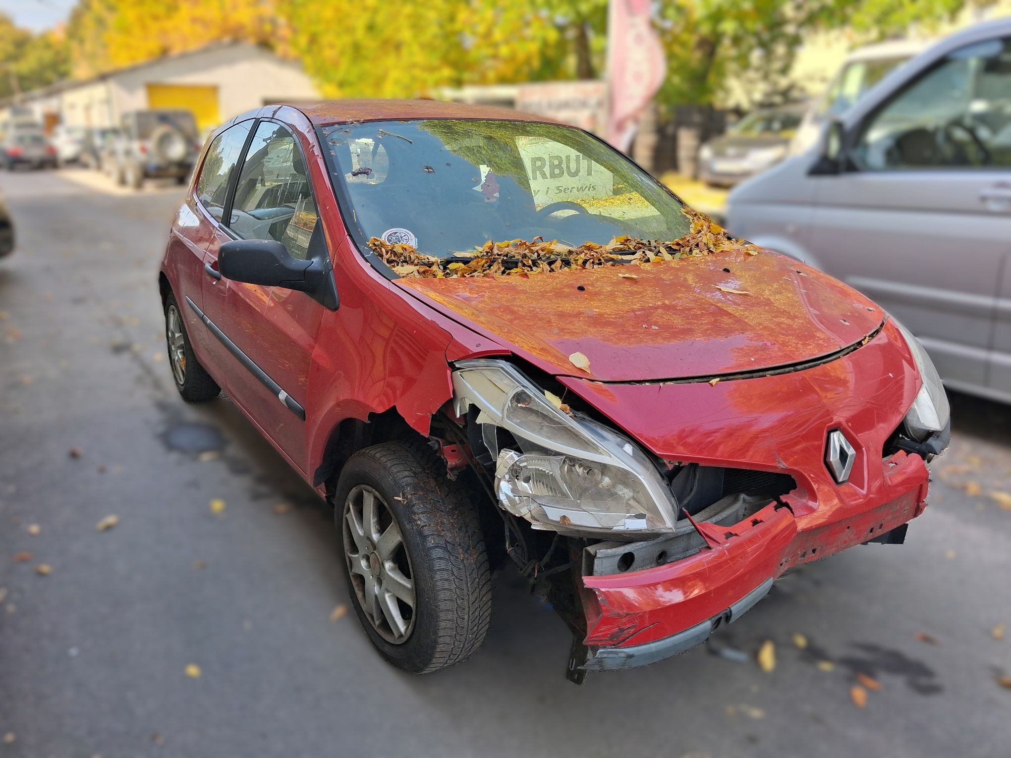 Czerwony samochód osobowy Renault z uszkodzonym przodem. Widoczne są zniszczone elementy maski, zderzaka i reflektorów