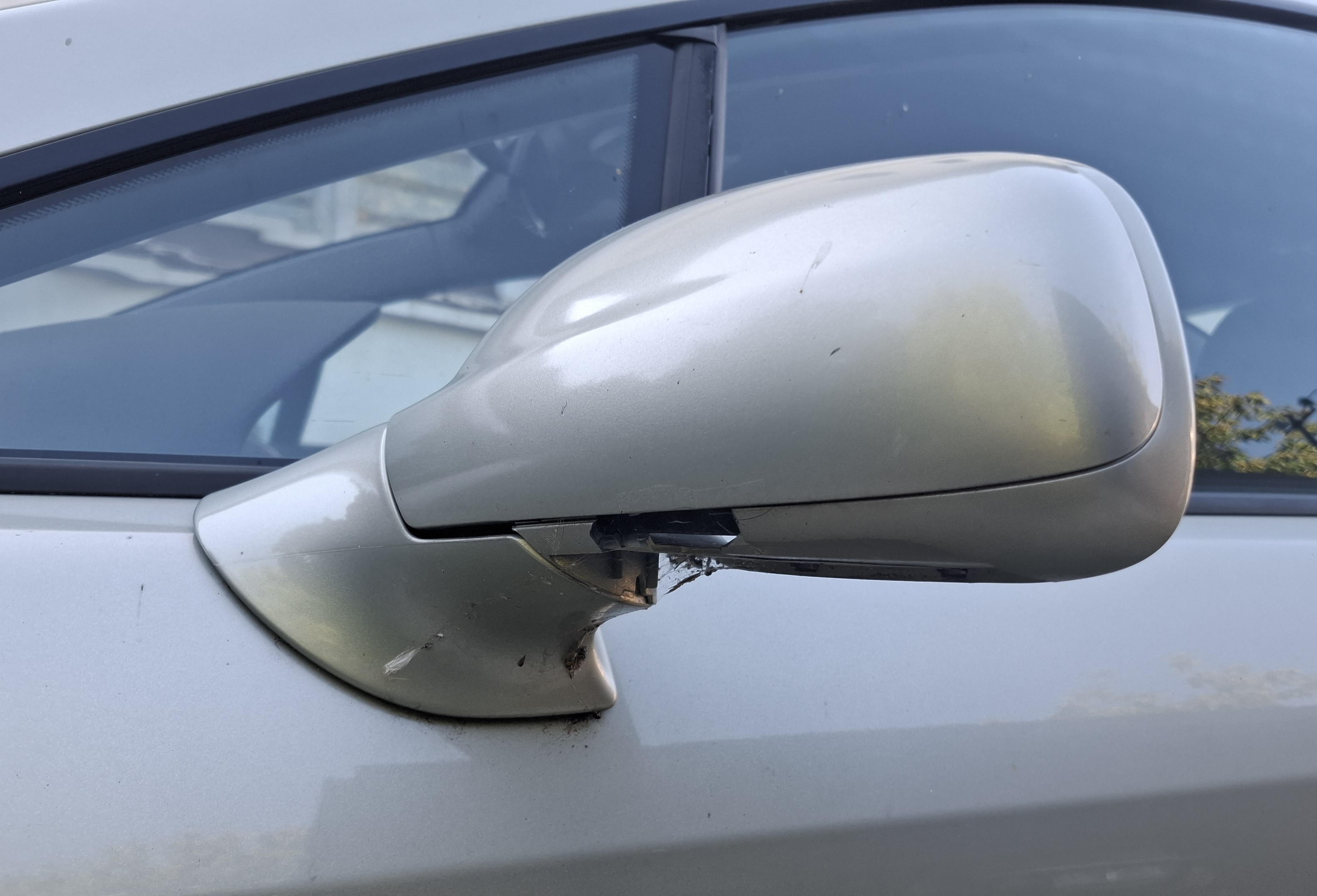 Zdjęcie przedstawia zbliżenie na prawe lusterko boczne. Widoczne jest pęknięcie i ubytek plastikowego elementu lusterka.